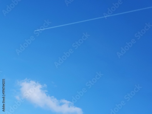 Condensation trail (contrail) in a blue sky, white streak forming behind a flying aircraft