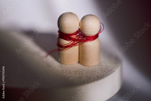 Wallpaper Mural Two wooden figurines tied together with red thread on a circular base, soft lighting creates a subtle shadow effect, emphasizing the connection between the figures Torontodigital.ca