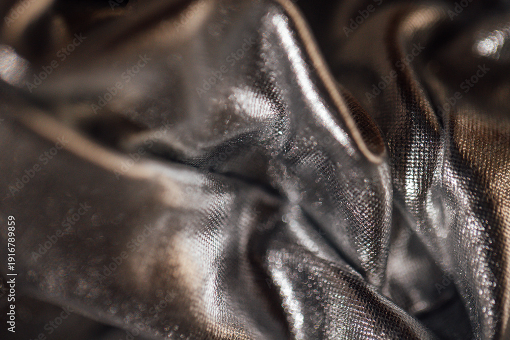 Obraz premium Close-up of crumpled black fabric with a shiny texture, showcasing intricate details and reflections under soft lighting, ideal for textile and fashion design applications