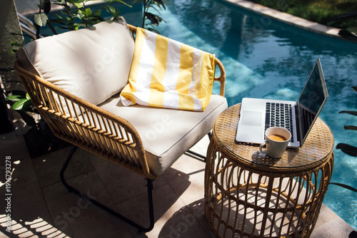 Wallpaper Mural Cozy outdoor seating area with a rattan chair, striped blanket, laptop, and coffee cup beside a swimming pool surrounded by lush greenery Torontodigital.ca