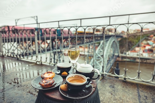 Savor a delightful spread of Portuguese pastries and coffee while overlooking the iconic Ponte Dom Luis I. A serene moment filled with culture on a rainy Porto day