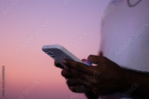 Person messaging on smartphone at sunset outdoors
