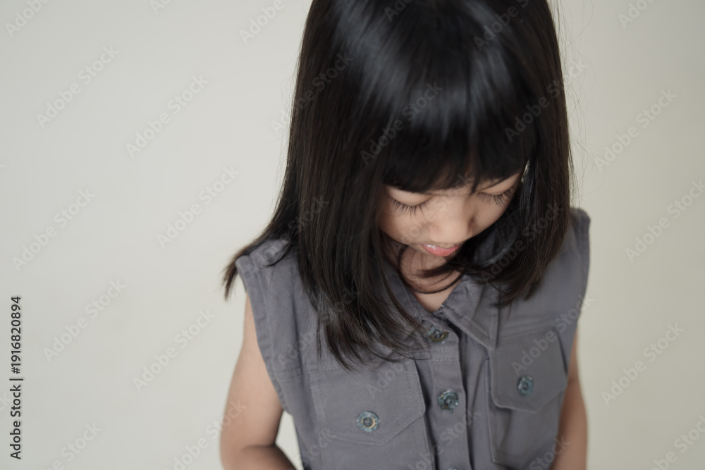 Fototapeta premium Asian little girl looking down wearing gray dress on neutral background, calm child portrait and kids fashion concept.