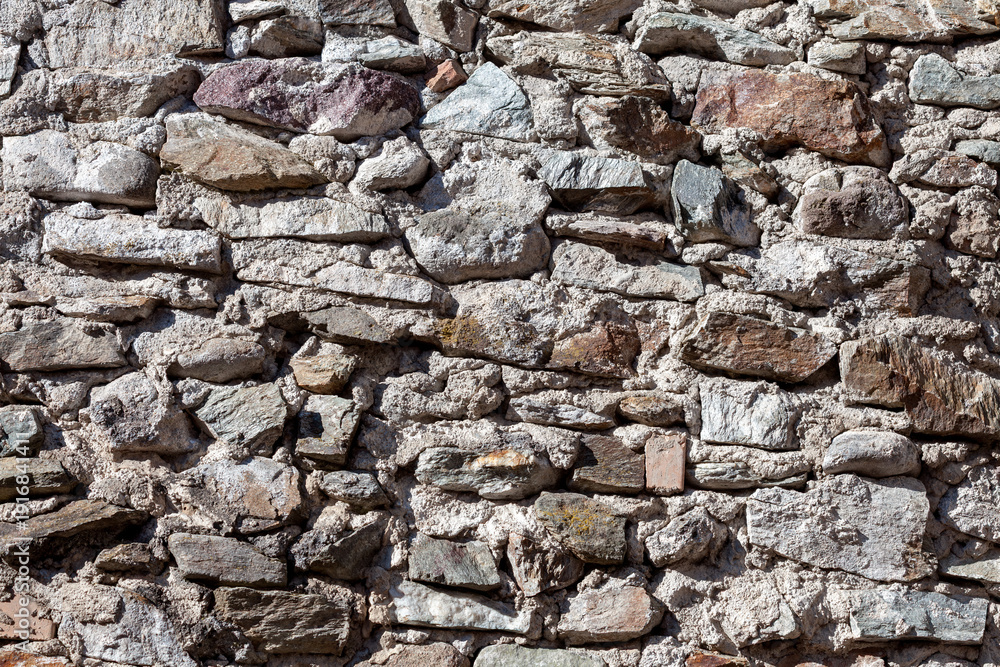 Obraz premium Close-up of a stone wall built with irregular rocks and mortar, suitable for architectural materials and natural textured backgrounds.