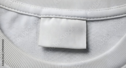 Blank white satin clothing tag sewn onto the neckline of a soft white fabric garment showing textured knit material detail and stitching construction up close.