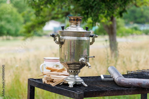 Fotografija The samovar stands on an iron table, outdoors, on a clearing in the forest Near