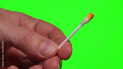 A used cotton swab against a green background.
Earwax on a cotton swab after use.
Close-up of earwax against a green isolated background.