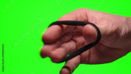 A man's hand stretches an elastic hair tie against a green background.
A black hair tie on a Chroma Key.