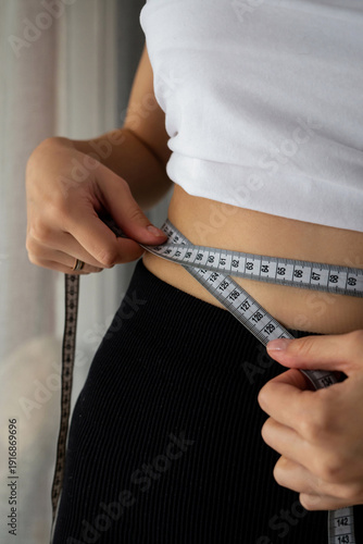 Woman measuring her waist with tape measure for Fitness and Weight Loss Progress.