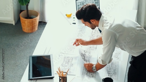 Canvas Print Architect engineer using laptop planning house design at office while sitting at meeting table with blueprint and equipment scatter around