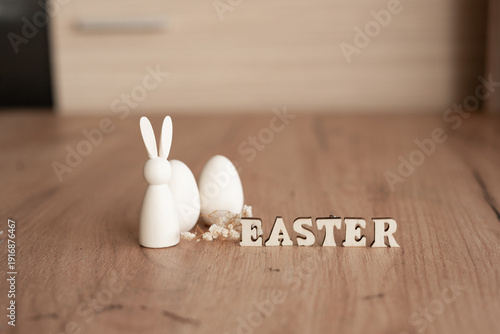 Minimal Easter still life on wooden floor with white bunny figurine, eggs and wooden letter blocks spelling easter, soft natural light, copy space. easter decor with bunny and eggs on wooden floor