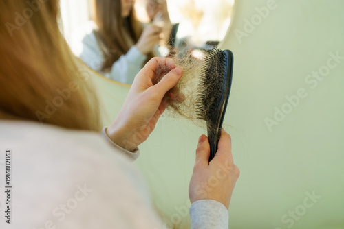 Canvas Print A woman is holding a black hairbrush filled with loose hair