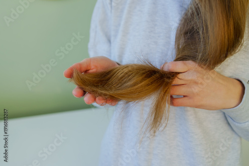 Obraz na plátně Close-up of hands holding long brown hair to inspect split ends, dryness and brittle texture