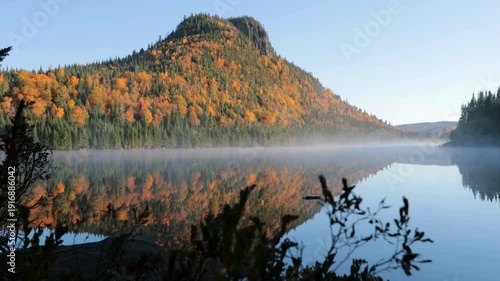 Mesmerizing view of mountain lake at dawn with autumn forest reflection. Serene view with colored peak and a soft layer of morning mist of nature.