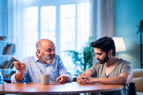 Indian Elderly dad guiding his grown son in a thoughtful family moment indoors.