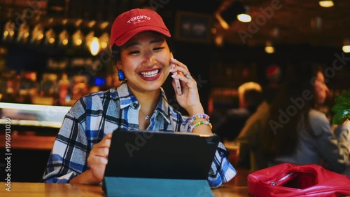Smiling Asian woman talking on smartphone in restaurant, ambitious female entrepreneur phoning near tablet, professional digital nomad having business conversation, career growth concept