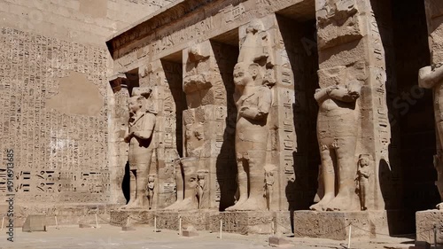 Medinet Habu temple first courtyard with Osiride pillars and Ramses III statues in mummy form in Luxor Egypt, hieroglyphic covered walls and ancient pharaonic colonnade.