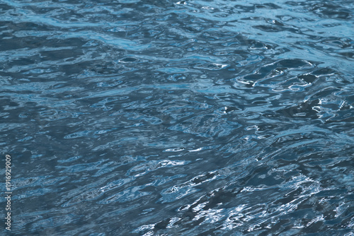 Blue rippling water surface with reflective highlights and waves forming an a...