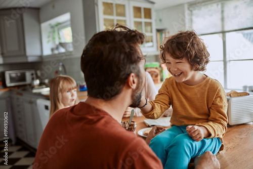 Slika na platnu Smiling child feeding dad with spoon in family kitchen