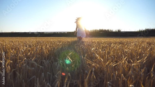 Young girl in a white dress running at a wheat field. Follow to unrecognizable woman jogging at the rye meadow. Blue sky with bright sunlight at background. Freedom concept. Slow Motion