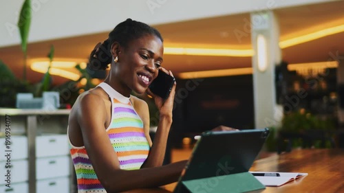 Successful African American woman talking on smartphone in modern office, ambitious female entrepreneur using digital tablet with stylus, professional freelancer having business conversation