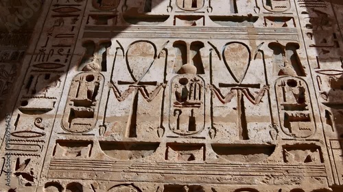 Closeup of ancient Egyptian hieroglyphic inscriptions with cartouches and bird symbols carved in sandstone wall at Medinet Habu temple in Luxor Egypt, detailed royal text.