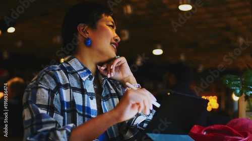 Dreamy Asian girl looking at tablet screen in cafe, happy student satisfied with online project, youthful digital nomad enjoying remote work, authentic representation of lifestyle and zen
