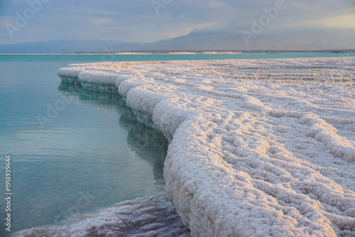 Obraz na plátne Thick salt crystal formations along calm turquoise water under soft evening light
