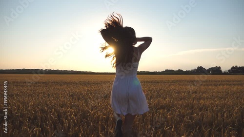 Beautiful girl is running along wheat field at sunset. Young woman jogging at the meadow and enjoing freedom. Summer leisure at nature concept. Close up Slow motion