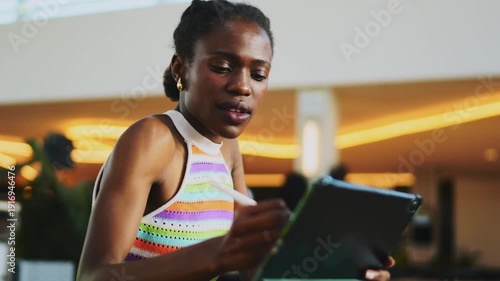 Joyful African American woman rejoices at success using digital tablet, happy female influencer chatting on phone in office, authentic representation of confidence and positive attitude