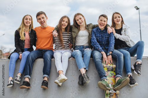 Принти на полотні Group of diverse teenagers sitting together at skatepark, smiling at camera, emb
