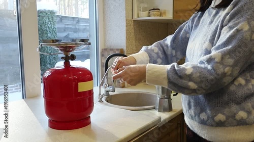 A young Ukrainian woman lights a gas stove with a match to make herself coffee during a power outage. The intimate kitchen scene highlights everyday resilience and adaptation to electricity shortages 
