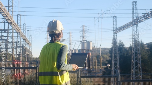 Photos Engineer wearing safety vest and hard hat, holding a laptop, standing with her b