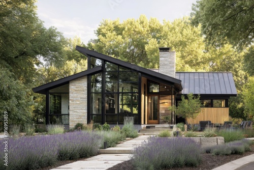 Modern house design with large windows and stone exterior in a green landscape during daytime near a garden path lined with lavender plants