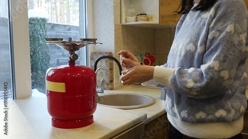 A young Ukrainian woman lights a gas stove with a match to make herself coffee during a power outage. The intimate kitchen scene highlights everyday resilience and adaptation to electricity shortages 