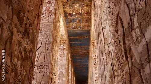 Medinet Habu temple colonnade with hieroglyphic inscriptions and relief carvings in Luxor Egypt, massive sandstone columns with papyrus capitals under dramatic blue sky.