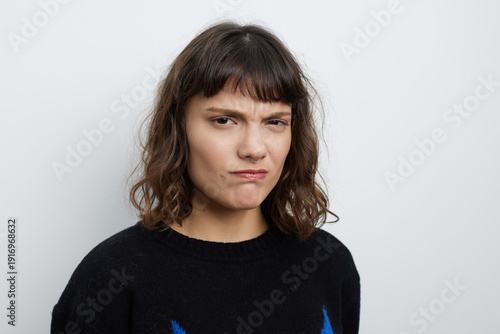 Fotografie Portrait of a young woman with a puzzled expression, wearing a dark sweater against a neutral studio backdrop