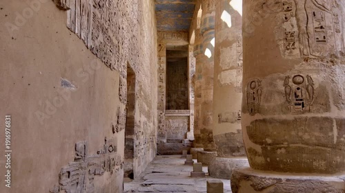 Medinet Habu temple colonnade with hieroglyphic inscriptions and relief carvings in Luxor Egypt, massive sandstone columns with papyrus capitals under dramatic blue sky.