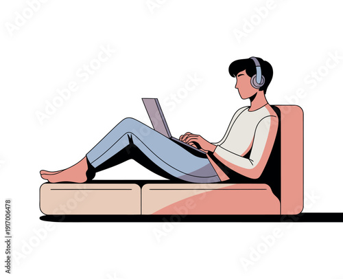 A young man relaxing on a couch while working on his laptop and listening to music with headphones