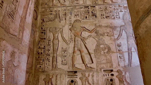 Medinet Habu temple colonnade with hieroglyphic inscriptions and relief carvings in Luxor Egypt, massive sandstone columns with capitals under dramatic blue sky.