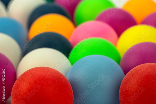 Colorful balls arranged closely together on a flat surface with various colors in the background during daylight