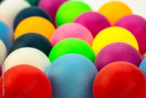 Colorful balls arranged closely together on a flat surface with various colors in the background during daylight