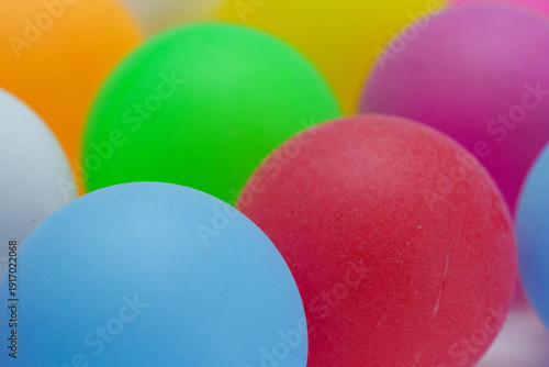 Colorful balls arranged closely together on a flat surface with various colors in the background during daylight