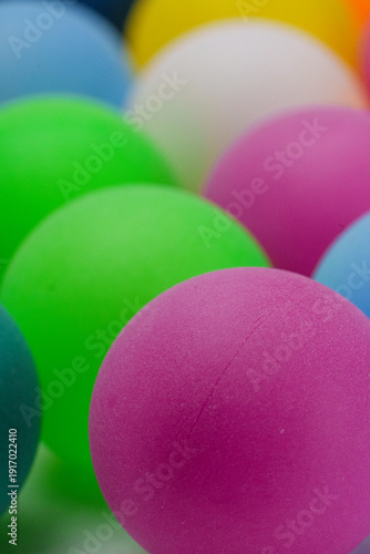 Colorful balls arranged closely together on a flat surface with various colors in the background during daylight