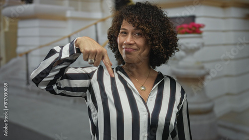 Photography Woman in striped shirt wearing gold pendant smiling with finger pointing to head on street; idea happiness