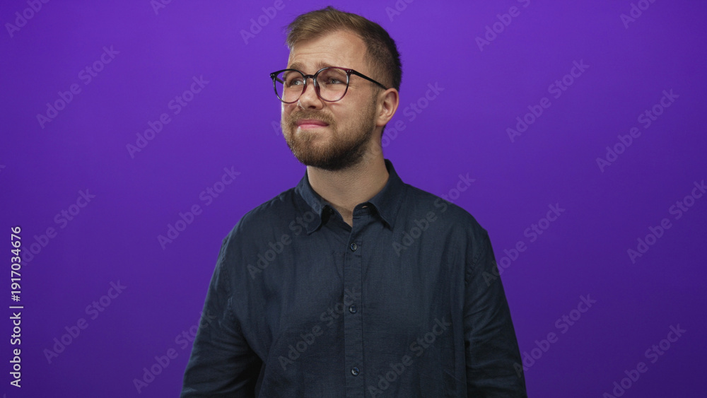Fototapeta premium Man wearing glasses and a button shirt with visible face looking up toward a light in purple studio; confusion.