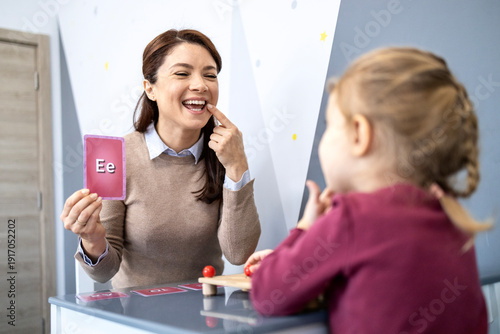 Speech therapist teaching child articulation and pronunciation using letter flashcard during a speech therapy session, focusing on speech development and language skills