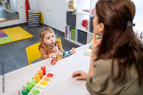 Speech therapist assisting a young girl with speech development, engaging in language lessons and communication therapy using educational toys in a school setting