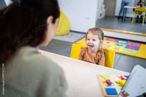 Speech therapist working with a happy little girl, helping her with early language development and educational therapy using engaging wooden puzzle games in a bright room