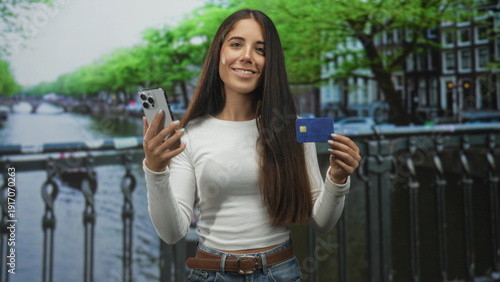 Wallpaper Mural Young woman holds creditcard and smartphone, showing card while checking phone on street; confidence convenience. Torontodigital.ca